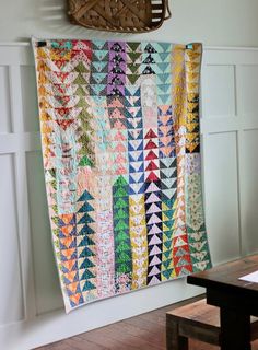 a colorful quilt hanging on the wall next to a wooden table with a basket above it