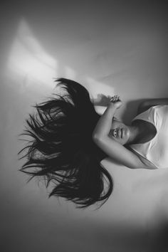 a woman laying on top of a bed with her hair blowing in the wind