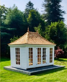 a small white gazebo sitting on top of a lush green field next to trees