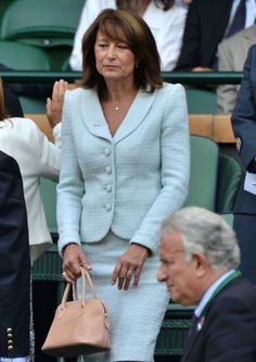 a woman in a light blue suit and matching handbag stands next to an older man