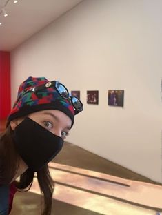 a woman wearing a black face mask in front of a wall with pictures on it