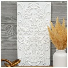 a vase with some dry grass in it next to a white wall paneling design