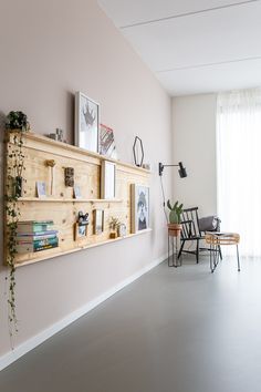 an empty room with some books and pictures on the wall next to a chair, table and window