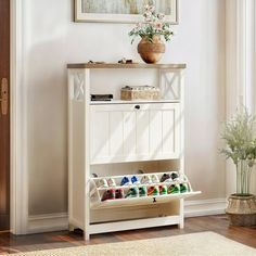 a white cabinet with drawers and baskets on top in front of a painting hanging on the wall