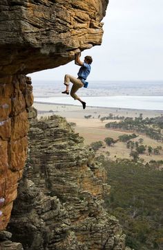 a man climbing up the side of a cliff with his feet in the air while holding onto a rope