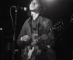 a man holding a guitar while standing in front of a microphone