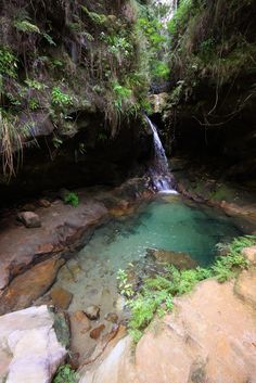 there is a small pool in the middle of some rocks and water with a waterfall coming out of it