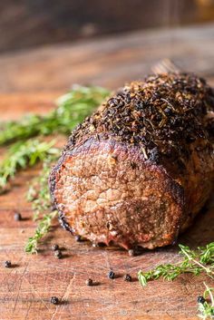 a piece of meat sitting on top of a wooden cutting board next to some herbs