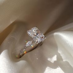 a diamond ring sitting on top of a white satin material covered in light shining from behind