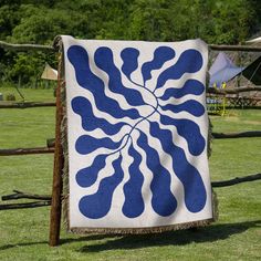 a blue and white quilt hanging on a wooden fence in front of a green field