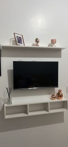 a flat screen tv mounted on a white wall next to shelves with vases and pictures