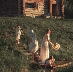 three women in white dresses are walking up the steps to a log cabin on a hill