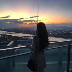 a woman standing on top of a tall building looking at the sunset over a city