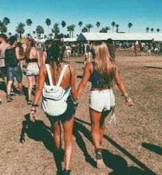 two women walking down the beach carrying backpacks on their backs, with palm trees in the background