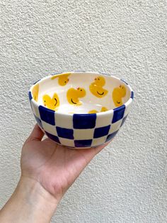 a hand holding a blue and white checkered bowl with rubber ducks on the side