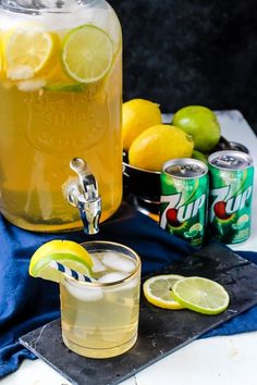 a pitcher of lemonade next to two cans of soda and limes on a table