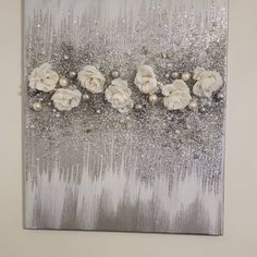 a painting with white flowers and silver glitters on the bottom, in front of a wall