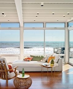 a living room filled with furniture and lots of windows overlooking the ocean on a sunny day