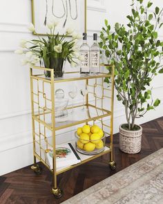 a gold bar cart with lemons and drinks on it next to a potted plant