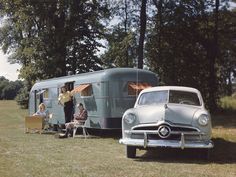 an old car is parked in front of a vintage camper and people are sitting at picnic tables