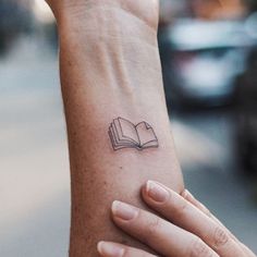 a woman's arm with a book tattoo on her left wrist and an open book in the middle