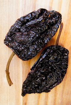 two dried black peppers sitting on top of a wooden cutting board