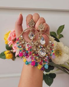 a woman's hand holding up some colorful jewelry and flowers in front of her