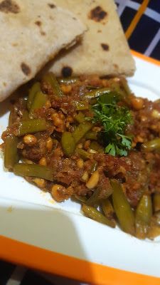 a white plate topped with green beans and meat next to pita bread on top of a checkered table cloth