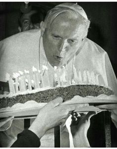 a man holding a cake with candles on it in front of another man's face