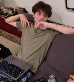 a man sitting on top of a couch next to a laptop computer