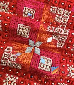 an orange and red quilt with white flowers on the bottom is laying on its side