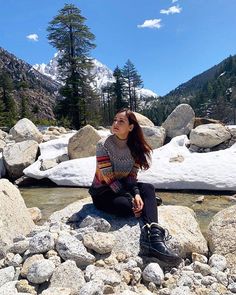 a woman sitting on top of a rock next to a river