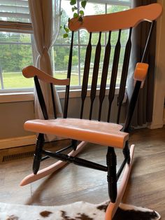 a wooden rocking chair sitting in front of a window next to a cowhide rug