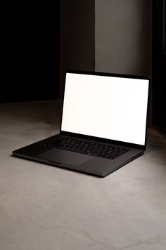 an open laptop computer sitting on top of a white table next to a black wall