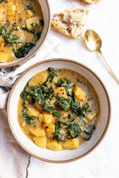 two bowls of soup with spinach, potatoes and bread on the side next to each other