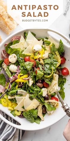 a white bowl filled with pasta salad and topped with tomatoes, olives, lettuce