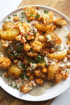 a white plate topped with potatoes covered in ranch dressing and garnished with parsley