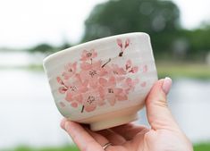 a hand holding a small white bowl with pink flowers on it