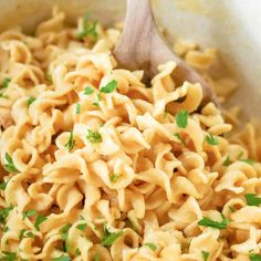 a wooden spoon full of macaroni and cheese with parsley on the side