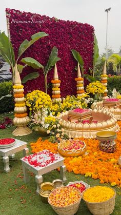 an arrangement of flowers in baskets and bowls on the grass near tables with trays of food