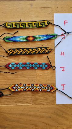 five beaded bracelets are laid out on a wooden table next to a piece of paper