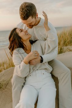 a man and woman sitting on top of each other in the sand at the beach