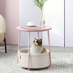 a cat sitting in a pink and white basket under a table next to a plant