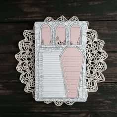 a pink and white paper with an ornate border around it on top of a wooden table