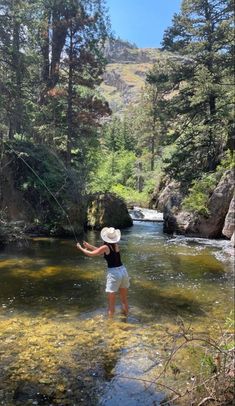 a woman standing in the middle of a river while holding onto a fishing line and wearing a hat