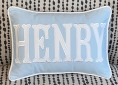 a blue and white pillow with the word henry on it sitting on a black and white patterned couch