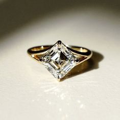 an engagement ring with a princess cut diamond in the center on a white table top