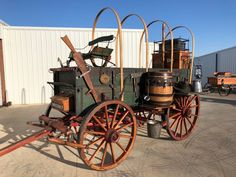 an old fashioned wagon is parked in front of a building with barrels on the wheels