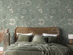 a bed with green sheets and pillows in front of a wallpapered bedroom area