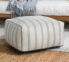 a white and blue striped ottoman sitting on top of a rug next to a bed